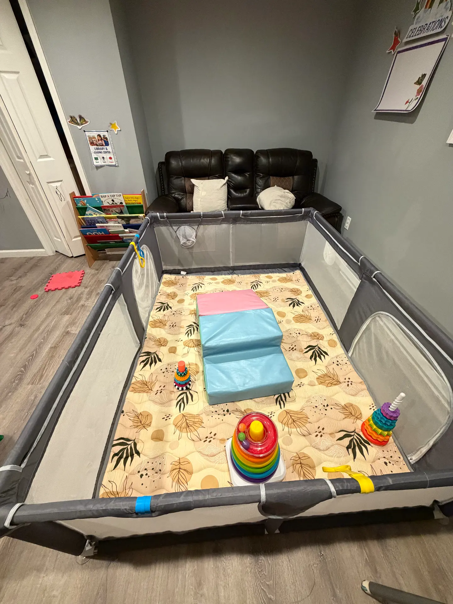 Large padded floor play space with stacking ring toys and a book rack nearby